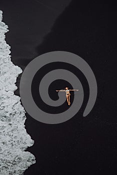 Woman laying on tropical beach black sand in white bikini