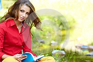 Woman lays on green field and reads book.