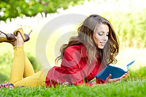 Woman lays on green field and reads book.