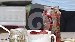 A woman lays sun-dried tomatoes in a jar of olive oil A woman pours olive oil over sun-dried tomatoes in a jar.Cooking sun-dried