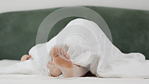 Woman lazily stretching lies in kingsize white bed. Female legs are showing from under blanket. Conept of relax and