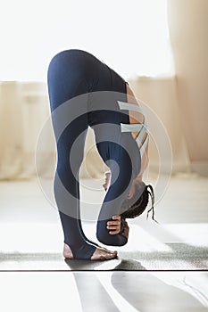 A woman leading a healthy lifestyle, exercising in sportswear, performs forward bends to stretch the muscles of the back and legs