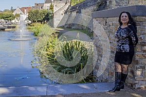 Woman leaning against a stone wall with a brook and fountain background