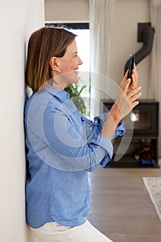Woman leaning against wall looking at cellphone at home