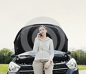 Woman leaning on the car and calling a car repair service