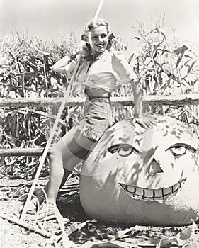 Woman leaning on large jack o'lantern on farm