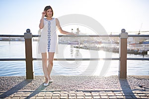 Woman leaning on railing next to water wearing summer dress