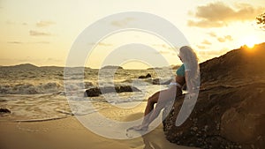 Woman leaning on a rock reef enjoying the warm golden sunset. Wo