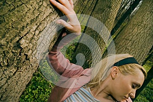 Woman leaning on tree trunk.