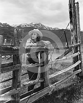 Woman leaning on wooden fence on ranch