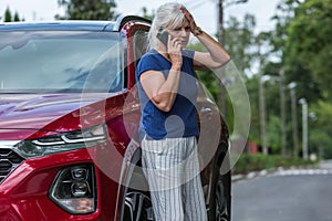 Woman leans against her red car and calls for help after causing an accident