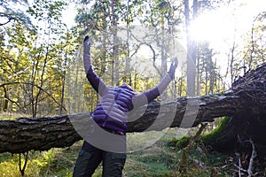Woman leans over fallen tree and rised her hands towards sun photo