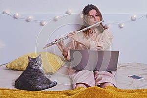 Woman learns music and cat, lifestyle. Girl plays the flute while sitting on yellow bed