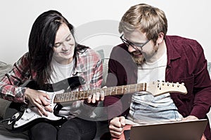 Woman learns to play the electronic guitar and she is pleased with successes, sitting next to a man who is very happy