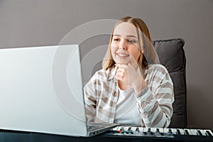 Woman learns to play piano online using laptop. Woman plays keyboard instrument on synthesizer piano during online lesson with