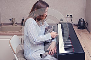 A woman learns to play the piano while sitting in a home kitchen next to a cat