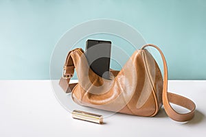 Woman leather handbag with phone and lipstick on table