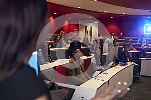 Woman lecturing students in lecture theatre, focus midground