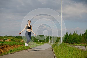 A woman in leggings and a tank top jumps on a rope on the street