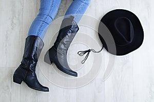 Woman legs in black cowboy boots with cowboy hat. Lying on a gray wooden background