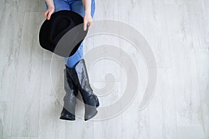 Woman legs in black cowboy boots with cowboy hat. Sitting on a gray wooden background