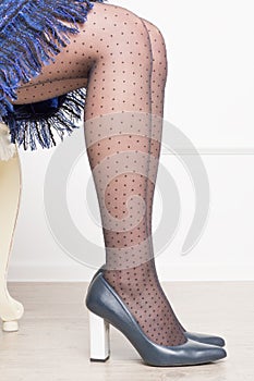 Woman legs in black tights in grid with polka dots in dark blue shoes with high heels