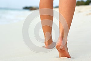 Woman legs and feet walking on the sand of the beach with the sea water in the background