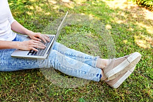 Woman legs on green grass lawn in city park, hands working on laptop pc computer. Freelance business concept
