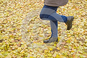 Woman legs with light blue jeans and black boots in orange autumn leaves