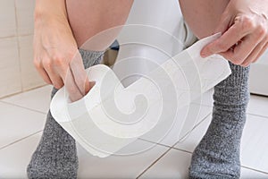 Woman legs in socks on a toilet with a roll of toilet paper in hands, digestive problems and defecation disorder concept