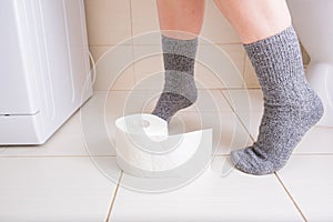 Woman legs in socks on a toilet with a roll of toilet paper in hands, digestive problems and defecation disorder concept