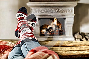 Woman legs with socks on wooden table and blurred fireplace in cozy home interior. Free space for your decoration.