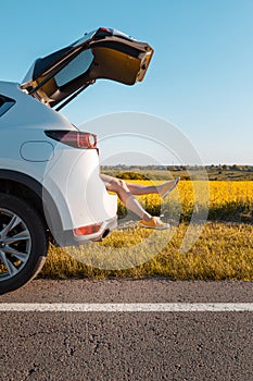 woman legs stick out of suv car trunk parked at roadside of speedway