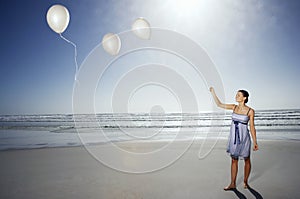 Woman Letting Go Of Balloons On Beach