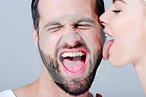 Woman licking face of shouting man isolated on grey