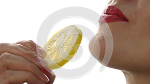 Woman licks and eating juicy lemon, close-up lips on a white background. slow motion