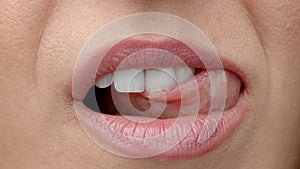 Woman licks her lips close up. Gentle female tongue licks beautiful white teeth.