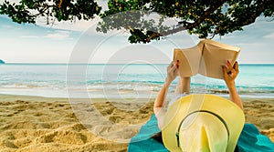 Woman lie down on green towel that put on sand beach under the tree and reading a book. Slow life on summer vacation. Asian woman photo