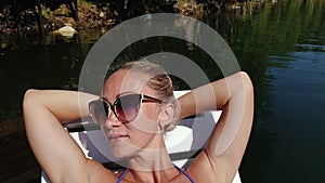 Woman lie on a sunbed in sunglasses and swimming suit. Girl rest on a flood wood underwater pier. Close up self portrait