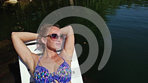 Woman lie on a sunbed in sunglasses and swimming suit. Girl rest on a flood wood underwater pier. Close up self portrait