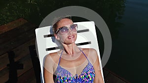 Woman lie on a sunbed in sunglasses and swimming suit. Girl rest on a flood wood underwater pier. Close up self portrait