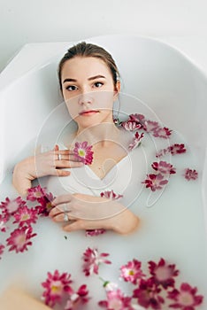 Woman lies in a bath with milk among the flowers