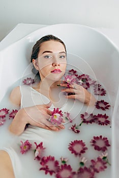 Woman lies in a bath with milk among the flowers