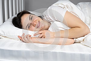 A woman lies in bed on her side on a pillow made of hollowfiber, hollow fiber