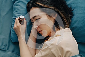 A woman lies in bed and holds antidepressant pills in her hands.