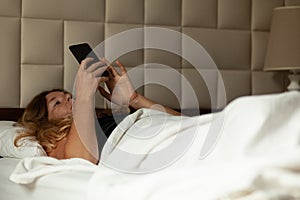Woman lies in bed with phone, internet addiction. Social network in smartphone
