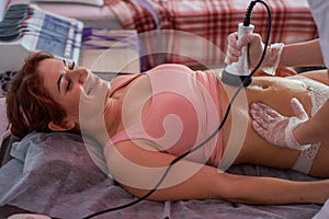 A woman lies on a couch and receives a hardware massage of the abdomen. The procedure for weight loss. Electric body