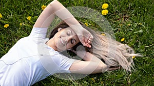 Woman lies on green grass, relaxing outdoors looking happy and smiling
