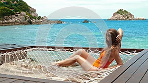 Woman lies in hammock on beach in tropical paradise.