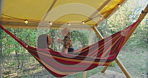 A woman lies in a hammock and holds a baby